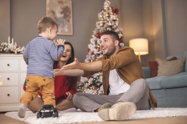 Genç ebeveynler Noel 'i evde yeni yürümeye başlayan çocuklarıyla birlikte geçiriyorlar, hediyeleri açıyorlar ve yeni oyuncaklarla oynuyorlar.