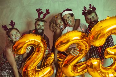 Bir grup genç arkadaş yeni yıl partisinde eğleniyor, dans ediyor ve gece yarısı geri sayımında 2023 numara şeklinde balonlar tutuyor.