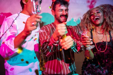 Bir grup neşeli genç arkadaş yılbaşı partisinde gece yarısı partisinde şampanya açarken eğleniyorlar.