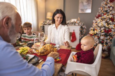 Mutlu çoklu nesil aile Noel 'i evde kutluyor, aile yemeği için masanın etrafında toplanıyor.