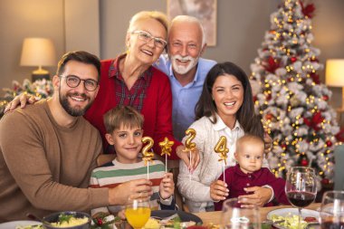 Mutlu çok nesilli aile, kış tatilini birlikte geçirmenin keyfini çıkarıyor, 2024 numaralı balonları tutarken, evde Noel yemeği yerken eğleniyor.