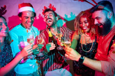 Bir grup neşeli genç arkadaş dans ediyor, kadeh kaldırıyor ve yılbaşı partisinde şampanya içiyor.