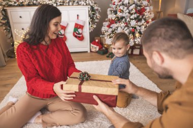 Genç ebeveynler Noel 'i evde birlikte geçirirken küçük çocuklarıyla birlikte Noel hediyelerini açarken eğleniyorlar.