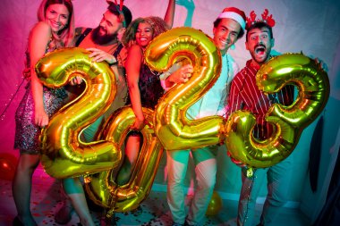 Bir grup genç arkadaş yeni yıl partisinde eğleniyor, dans ediyor ve gece yarısı geri sayımında 2023 numara şeklinde balonlar tutuyor.