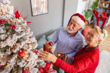 Yılbaşı ağacını süsleyen ve kış tatilinde evde eğlenen mutlu çiftin yüksek açılı görüntüsü.