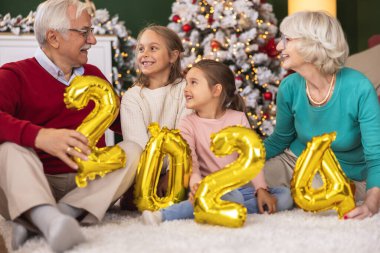 Güzel, mutlu, çoklu kuşak bir aile evde yeni yılı kutluyor, dedelerle nineler torunlarıyla vakit geçiriyor, ellerinde 2024 balon tutuyor.