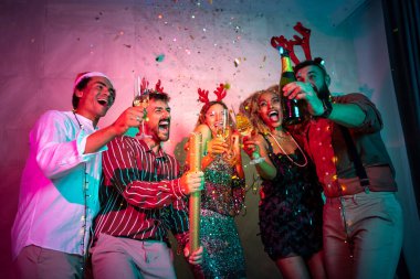 Arkadaşlar yeni yıl partisinde eğleniyor, dans ediyor, şarkı söylüyor, konfeti atıyor ve gece yarısı şampanya içerken kadeh kaldırıyor. Ortadaki şampanya kadehlerine odaklan.