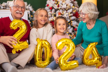 Güzel, mutlu, çoklu kuşak bir aile evde yeni yılı kutluyor, dedelerle nineler torunlarıyla vakit geçiriyor, ellerinde 2024 balon tutuyor.