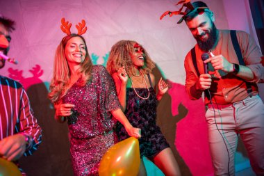 Bir grup neşeli genç arkadaş yeni yıl partisinde karaoke söyleyip dans ederek eğleniyorlar.