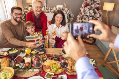 Güzel, mutlu, çok nesilli bir aile masanın etrafında toplandı. Son sınıf öğrencisi, Noel yemeğini evde yerken ailesinin fotoğraflarını çekiyor.