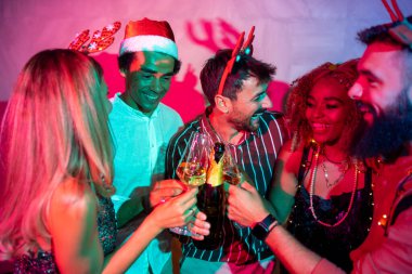 Bir grup neşeli genç arkadaş kadeh kaldırarak eğleniyor ve yılbaşı partisinde şampanya içiyorlar.