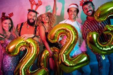 Bir grup genç arkadaş yeni yıl partisinde eğleniyor, dans ediyor ve gece yarısı geri sayımında 2023 numara şeklinde balonlar tutuyor.