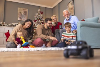 Mutlu çoklu nesil aile Noel 'i evde birlikte geçiriyorlar, baba oğluna uzaktan kumandalı oyuncak arabayla nasıl oynanacağını öğretiyor.