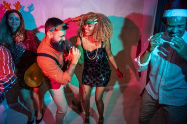 Bir grup neşeli genç arkadaş yeni yıl partisinde karaoke söyleyip dans ederek eğleniyorlar.