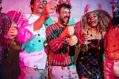 Bir grup neşeli genç arkadaş yılbaşı partisinde şampanya açıp dans ederek eğleniyor.