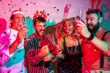 Bir grup neşeli genç arkadaş yılbaşı partisinde bir şişe şampanya açıp dans ederek eğleniyorlar.