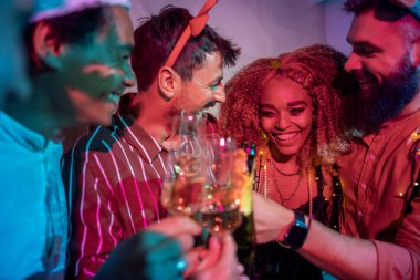 Bir grup neşeli genç arkadaş kadeh kaldırarak eğleniyor ve yılbaşı partisinde şampanya içiyorlar.