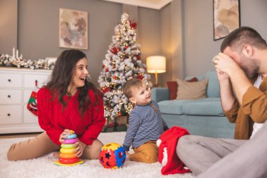 Genç ebeveynler Noel 'i evde birlikte geçirirken küçük çocuklarıyla birlikte Noel hediyelerini açarken eğleniyorlar.