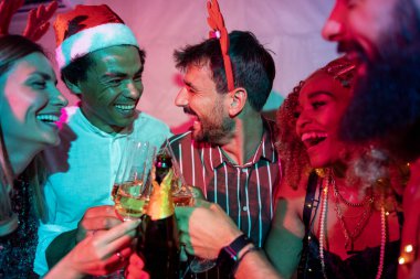 Bir grup neşeli genç arkadaş kadeh kaldırarak eğleniyor ve yılbaşı partisinde şampanya içiyorlar.