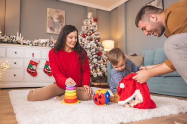 Genç ebeveynler Noel 'i evde birlikte geçirirken küçük çocuklarıyla birlikte Noel hediyelerini açarken eğleniyorlar.