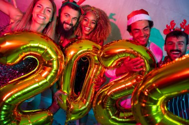 Bir grup genç arkadaş yeni yıl partisinde eğleniyor, dans ediyor ve gece yarısı geri sayımında 2024 numara şeklinde balonlar tutuyor.