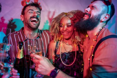 Bir grup neşeli genç arkadaş dans ediyor, kadeh kaldırıyor ve yılbaşı partisinde şampanya içiyor.