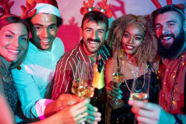Bir grup neşeli genç arkadaş kadeh kaldırarak eğleniyor ve yılbaşı partisinde şampanya içiyorlar.