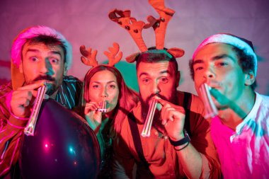 Bir grup neşeli genç arkadaş yeni yıl partisinde parti düdüğü çalarken eğleniyorlar.