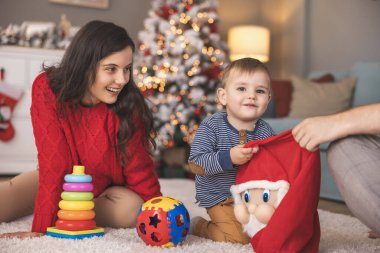 Genç ebeveynler Noel 'i evde birlikte geçirirken küçük çocuklarıyla birlikte Noel hediyelerini açarken eğleniyorlar.