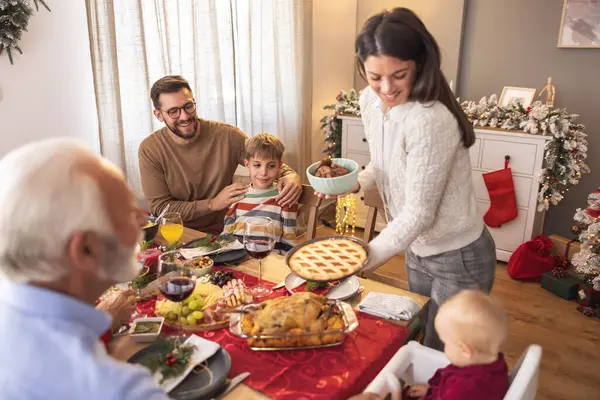 Aile, Noel yemeğini evde yerken masanın etrafında toplandı. Genç bir kadın tatlı olarak elmalı turta ve kurabiye getirdi.