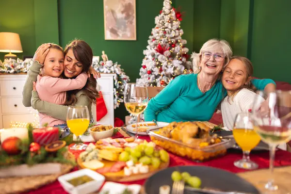 Çok nesildir evde Noel yemeği yiyen aile, masanın etrafında toplanmış, anne, kız ve torunlar birlikte vakit geçiriyorlar, sarılıyorlar ve öpüşüyorlar.