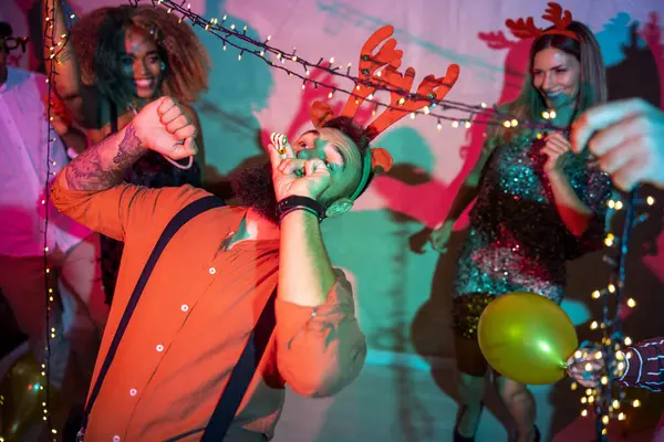 Bir grup neşeli genç arkadaş yılbaşı partisinde yılbaşı ışıklarının altında dans ederek eğleniyorlar.