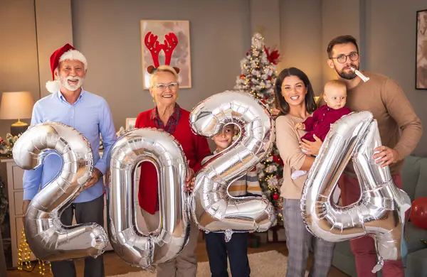 Güzel mutlu bir aile Noel 'i evde kutluyor, 2024 numaralı dev balonları tutarak eğleniyor, gelecek yeni yılı temsil ediyor.