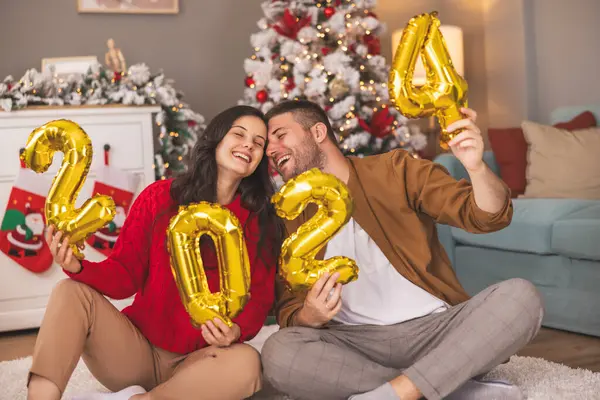 Güzel, genç ve aşık bir çift kış tatili için evi dekore ederken ellerinde 2024 numaralı balonlar olacak.