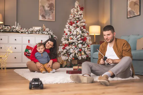 Genç ebeveynler, Noel 'i evde birlikte geçirirken hediyelerini açarken ve çocuklarıyla oynarken eğleniyorlar.