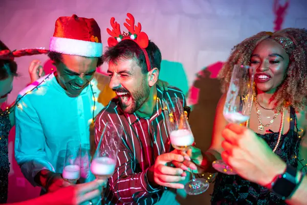 Bir grup neşeli genç arkadaş kadeh kaldırarak eğleniyor ve yılbaşı partisinde şampanya içiyorlar.