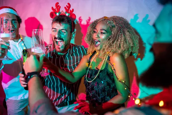 Bir grup neşeli genç arkadaş kadeh kaldırarak eğleniyor ve yılbaşı partisinde şampanya içiyorlar.