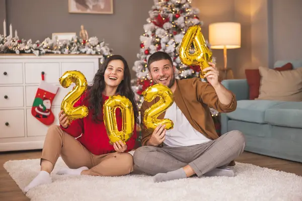 Güzel, genç ve aşık bir çift kış tatili için evi dekore ederken ellerinde 2024 numaralı balonlar olacak.