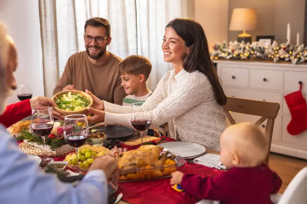 Mutlu çoklu nesil aile masanın etrafında toplandı, evde hep birlikte Noel yemeği yiyorlar, tabakları birbirlerine veriyorlar ve tabağa yemek koyuyorlar.