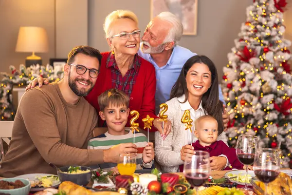 Mutlu çok nesilli aile, kış tatilini birlikte geçirmenin keyfini çıkarıyor, 2024 numaralı balonları tutarken, evde Noel yemeği yerken eğleniyor.