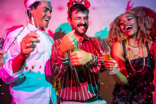 Bir grup neşeli genç arkadaş yılbaşı partisinde gece yarısı partisinde şampanya açarken eğleniyorlar.