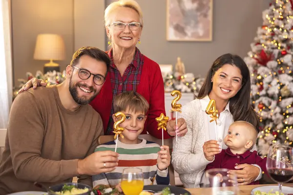 Mutlu çok nesilli aile, kış tatilini birlikte geçirmenin keyfini çıkarıyor, 2024 numaralı balonları tutarken, evde Noel yemeği yerken eğleniyor.