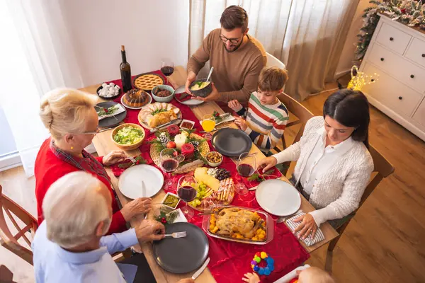 Masanın etrafında toplanmış mutlu, mutlu, çok nesilli aile manzarası, evde hep birlikte Noel yemeği yiyor, birbiriyle konuşuyor ve gülüyor.