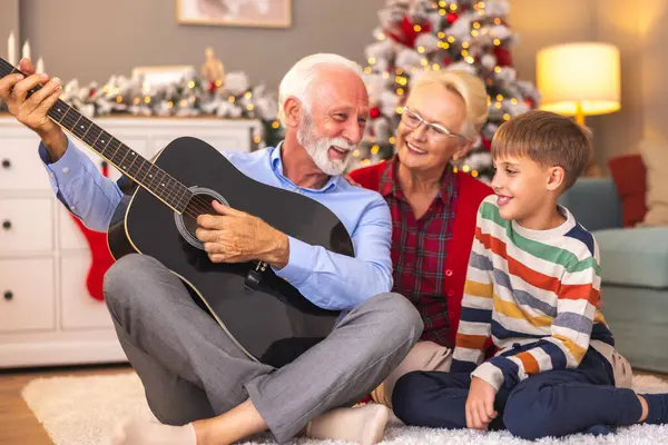Küçük çocuk kış tatilini büyükannesi ve büyükbabasıyla geçirirken, büyükbabası gitar çalarken karısı ve torunu Noel günü evde şarkı söylerken eğleniyor.