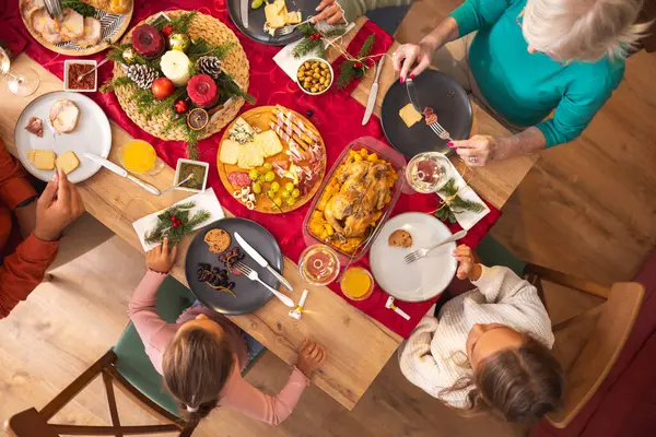 Masanın etrafında toplanmış mutlu, mutlu, çok nesilli aile manzarası, evde hep birlikte Noel yemeği yiyor, birbiriyle konuşuyor ve gülüyor.