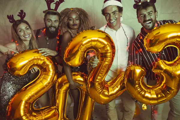 Bir grup genç arkadaş yeni yıl partisinde eğleniyor, dans ediyor ve gece yarısı geri sayımında 2023 numara şeklinde balonlar tutuyor.
