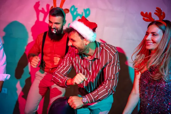 Bir grup neşeli genç arkadaş yeni yıl partisinde dans edip şarkı söylüyor.