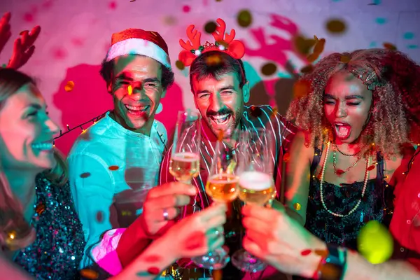 Bir grup neşeli genç arkadaş kadeh kaldırarak eğleniyor ve yılbaşı partisinde şampanya içiyorlar.