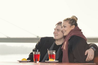 Birbirine aşık bir çift, sonbahar güneşli bir günde nehir kenarındaki bir kafede oturur çay içer, sarılır ve dinlenir. 