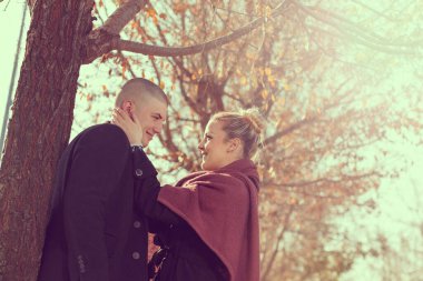 Birbirine aşık genç çift bir sonbahar tatilinde bir ağacın yanında duruyor doğanın tadını çıkarıyor, sarılıyorlar.